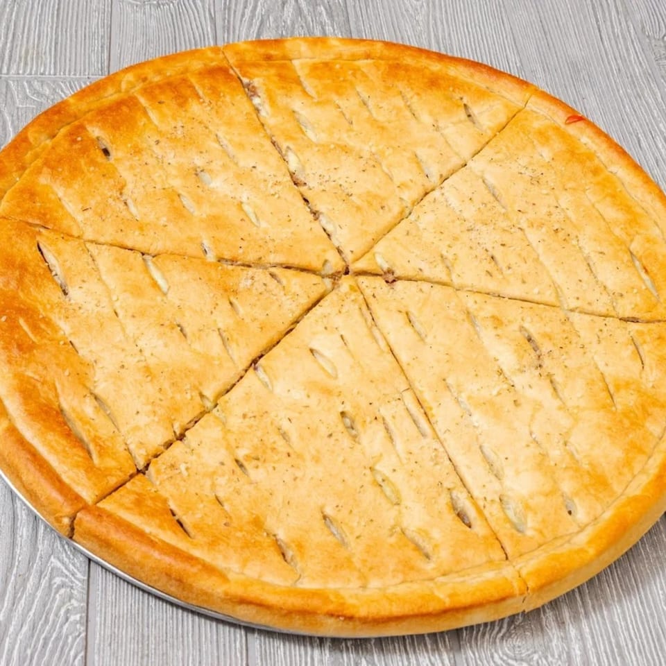 A golden-brown, sliced Bravo Pizza pie with a lattice crust on a gray wooden surface.