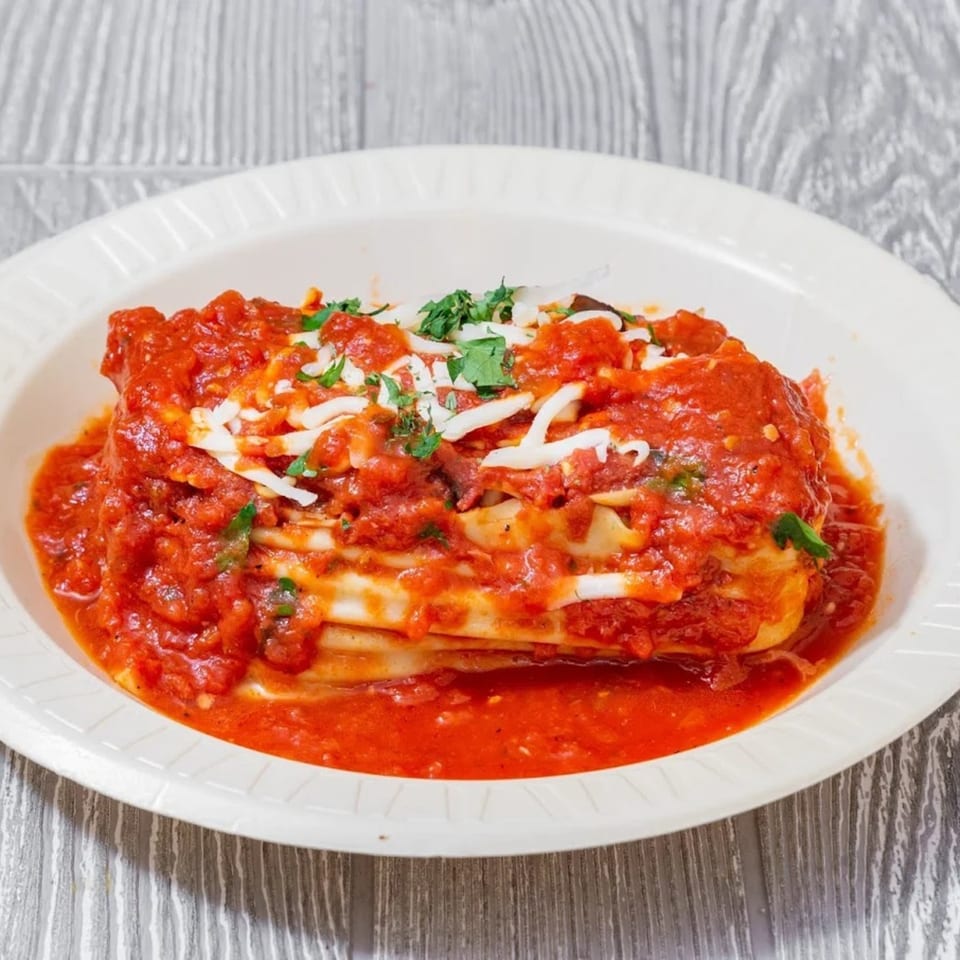 A serving of lasagna topped with rich red sauce, shredded cheese, and fresh parsley in a white bowl.