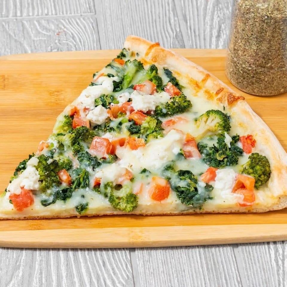 A slice of Bravo Pizza's white pizza with broccoli, spinach, tomatoes, and ricotta cheese.