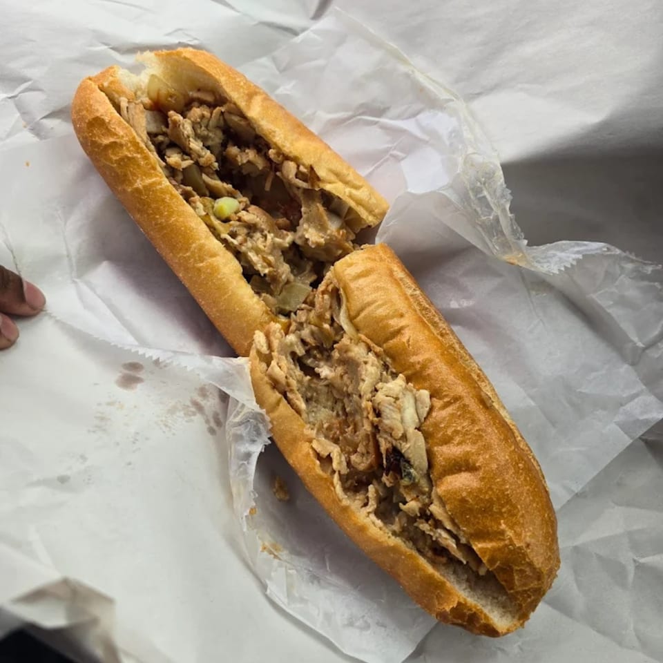 A chicken cheesesteak sandwich, cut in half, wrapped in white paper.