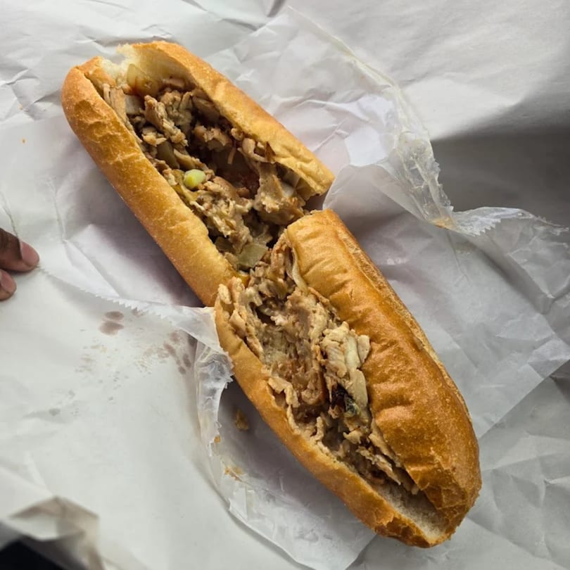 A chicken cheesesteak sandwich, cut in half, wrapped in white paper.