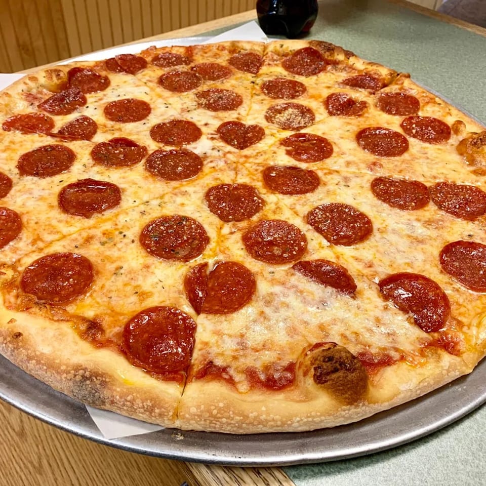 A whole pepperoni pizza with melted cheese and a heart-shaped pepperoni, on a metal tray.