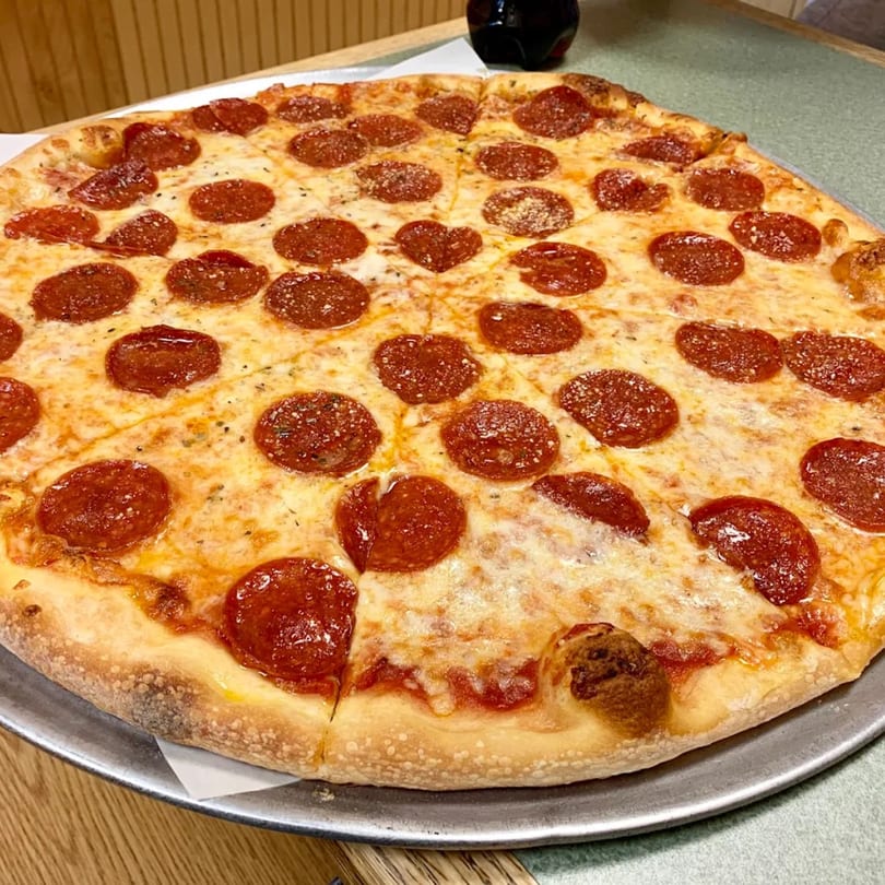 A whole pepperoni pizza with melted cheese and a heart-shaped pepperoni, on a metal tray.